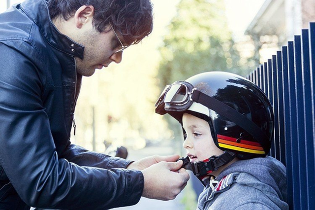Bố mẹ cho trẻ đội mũ bảo hiểm trước khi ngồi lên xe máy.