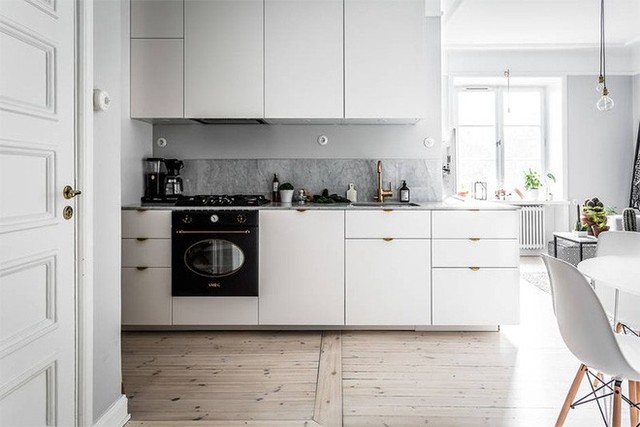 
Góc bếp được đặt ngay cạnh bức tường gần lối vào. Hệ thống tủ bếp đều được chọn màu trắng đơn giản, nổi bật trên nền tường màu ghi và tạo nên vẻ đẹp trẻ trung, hiện đại trên nền sàn gỗ quen thuộc, ấm cúng.
