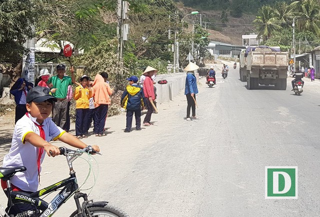 Bác bảo vệ Nguyễn Văn Châu giơ tấm biển Stop ra hiệu cho các xe tải đi chậm để dắt học sinh qua đường
