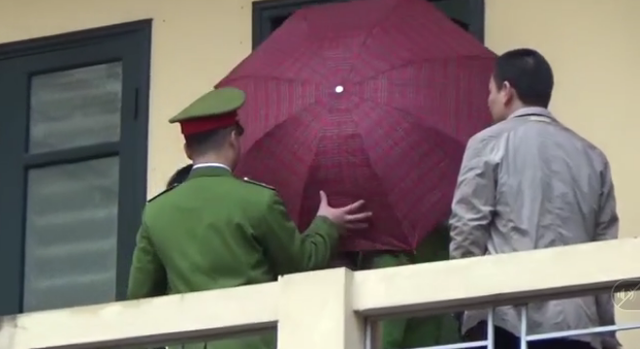 
Cảnh sát che ô khi dẫn giải bị cáo Đinh La Thăng rời phòng xử án.
