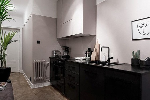 Không gian bếp với màu sắc trung tính, tủ bếp cùng tông màu tường, đồ nội thất từ kệ nấu nướng đến bếp, lò nướng, chậu cây trang trí đều sử dụng màu đen.