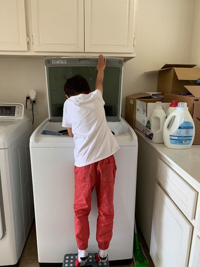 Hình ảnh Jacky tự giặt đồ, sấy đồ và lấy đồ ra. Chiếc máy giặt rất cao nên cậu bé phải bắc ghế để đứng lên.