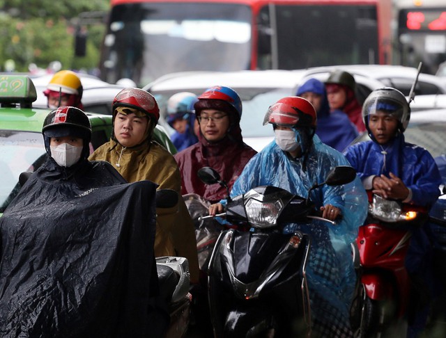 Người dân di chuyển bằng xe máy đứng chờ đèn đỏ dưới cơn mưa tại ngã tư Khuất Duy Tiến - Lê Văn Lương.