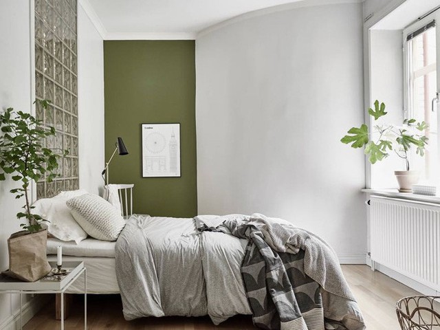 
Phòng ngủ nhiều ánh sáng với khung cửa đầy nắng in bóng cây xanh. Giường ngủ được đặt ngay cạnh tường vuông góc có màu xanh xám bình yên, tĩnh tại.
