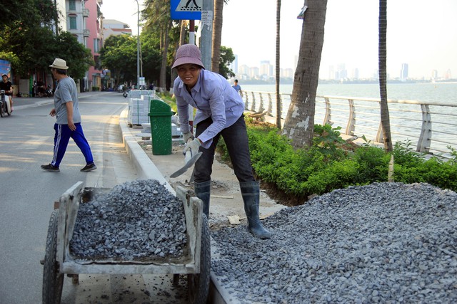 Chị Tân (47 tuổi) vừa nhanh tay xúc từng xẻng đá nghiền lên xe đẩy tay, để công nhân kịp trộn phục vụ công trình cải tạo, chỉnh trang hè phố bằng đá tự nhiên, ở phố Trích Sài (quận Tây Hồ, Hà Nội). Mặc dù mới bắt đầu cho ca làm việc thứ hai trong ngày và để tránh tác động từ nắng nóng, bà Tân tìm cách bảo vệ mình dưới bóng râm. Thế nhưng, nắng gắt lúc đầu giờ chiều kèm theo hơi nóng hầm hập hắt lên từ mặt đường, bà Tân cũng không tránh khỏi cảm giác lừ đừ, uể oải.