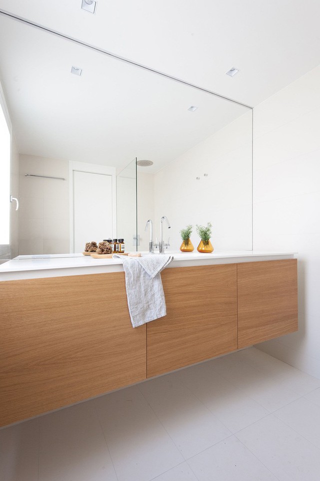 
Phòng tắm màu trắng sạch sẽ, ngăn nắp với kệ gỗ có ngăn lưu trữ rộng.
