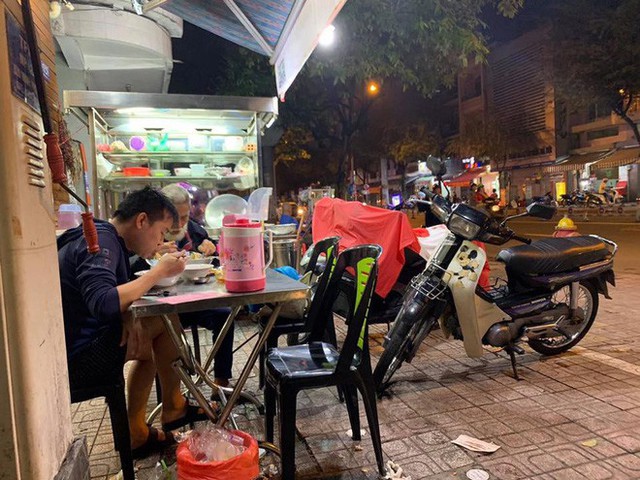 
Thanh niên ngồi ăn cùng cụ già bán vé số.
