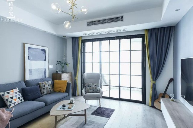 
Phòng khách được thiết kế đan xen màu xanh đậm và màu nhấn là vàng để tăng thêm cảm giác ấm cúng, sinh động cho ngôi nhà. Bộ sofa được chọn màu ghi đặt sát tường, bên cạnh là tấm thảm xinh xắn giúp bàn trà nhỏ trở nên nổi bật.
