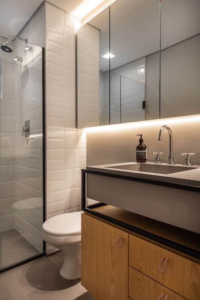 
Phòng tắm màu trắng với những điểm nhấn màu đen, bàn trang điểm bằng gỗ, bồn rửa bê tông và tủ gương lớn.
