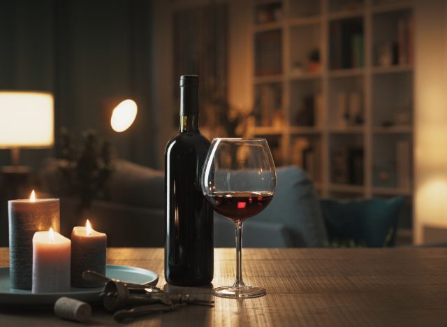 mũ ngủ, chai rượu vang đỏ và ly trên bàn cạnh nến