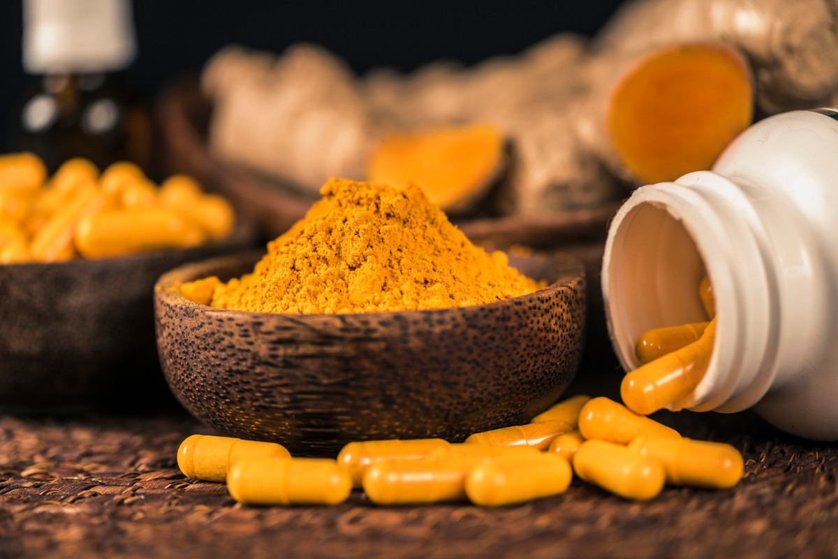 Viên nang bổ sung curcumin, bột nghệ trong bát thủy tinh và rễ nghệ làm nền.