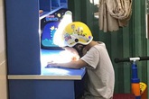 Sự thật đằng sau cảnh học sinh lớp 1 phải đội mũ bảo hiểm ngồi làm bài tập khi bố mẹ đứng cạnh Sự thật đằng sau cảnh học sinh lớp 1 phải đội mũ bảo hiểm ngồi làm bài tập khi bố mẹ đứng cạnh