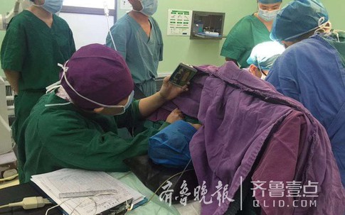Y tá ân cần quỳ bên bàn mổ suốt cả tiếng đồng hồ để cầm điện thoại cho bệnh nhi xem hoạt hình